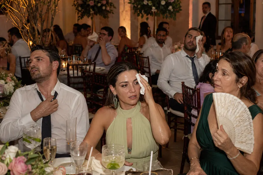 Convidados de um evento noturno com calor, se abanando e enxugando o suor